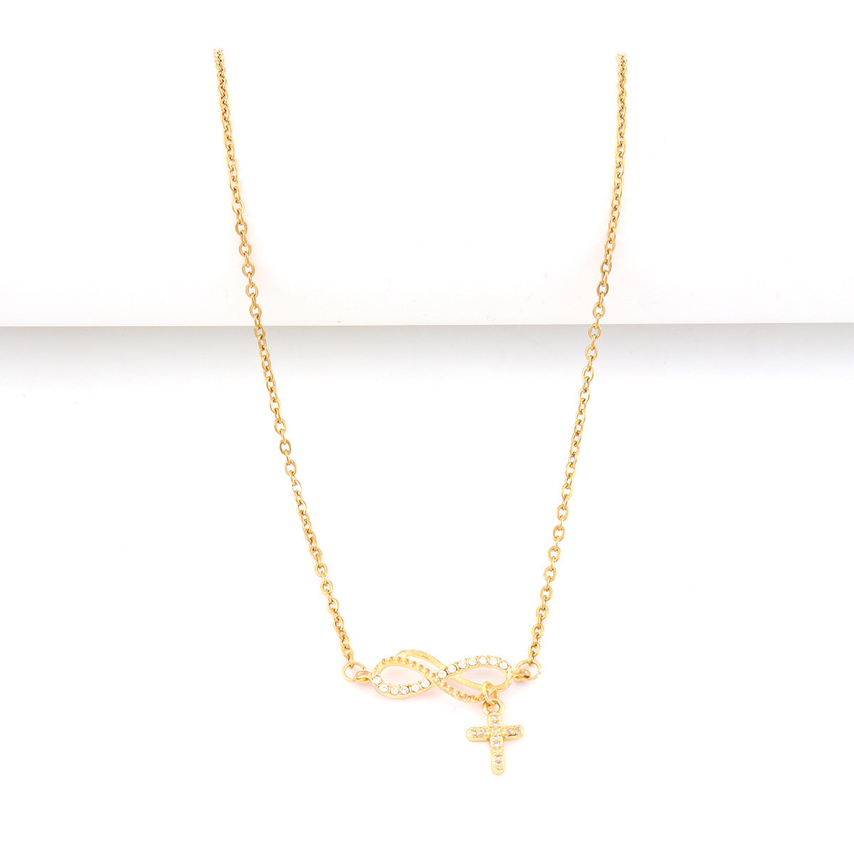 A delicate gold chain necklace featuring an infinity symbol and a small cross pendant, both adorned with tiny clear stones, displayed against a clean white background.