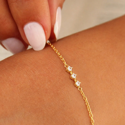 Gold bracelet with small diamonds on a wrist against a neutral background