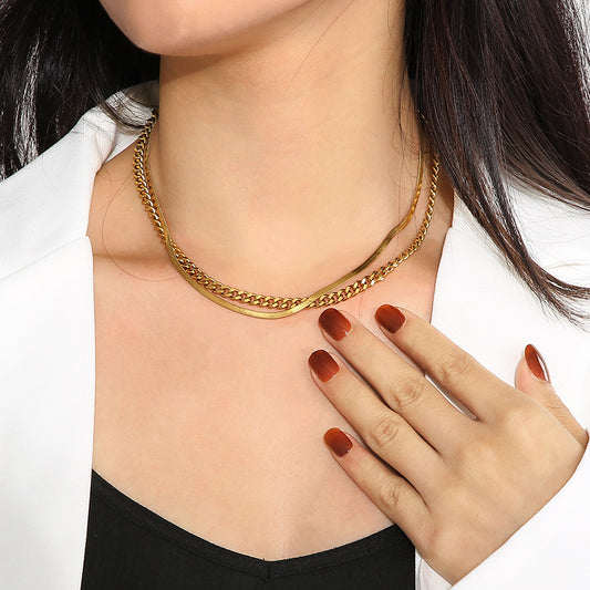 A close-up of a model wearing a double-layered gold chain necklace, styled with a white blazer and black top.